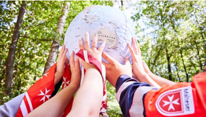 Several hands lift a globe together in a sunlit forest, symbolizing unity.