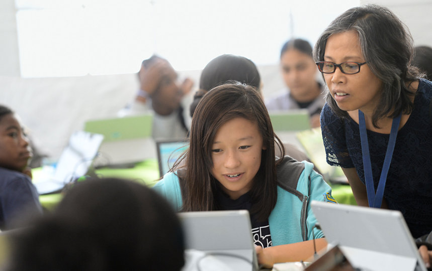 A teacher leans in to help a student working