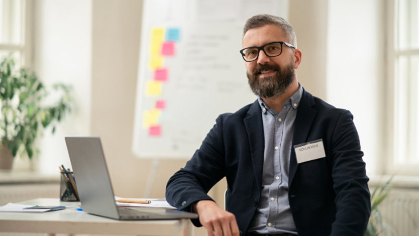 A person with a volunteer badge, sitting at a desk with a computer.