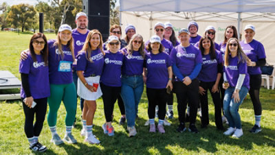 A cheerful group of volunteers in matching purple shirts pose at an outdoor event.