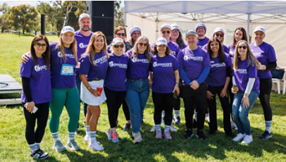 A cheerful group of volunteers in matching purple shirts pose at an outdoor event.