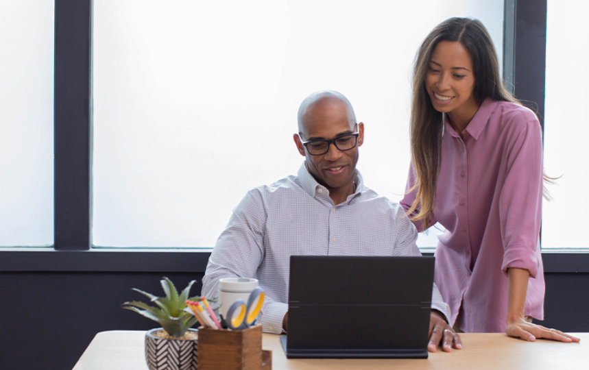 In an office, two coworkers gaze at a laptop's display.