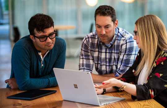 In an office, a woman shows her two coworkers what is on her laptop.