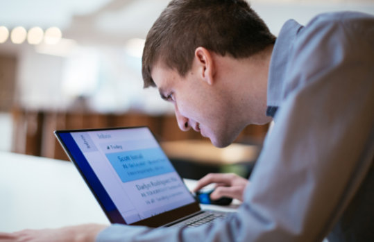 A man who has low vision looks closely at a laptop screen as he reads text in big font.