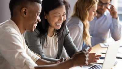 A happy mature woman discussing a project on a laptop with a young colleague.