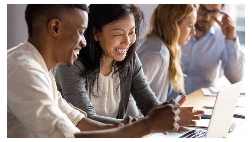 A happy mature woman discussing a project on a laptop with a young colleague.