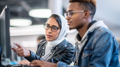 A female helps a man with a project on a computer screen.