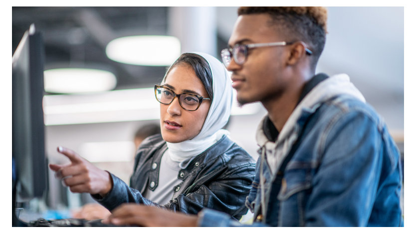 A female helps a man with a project on a computer screen.