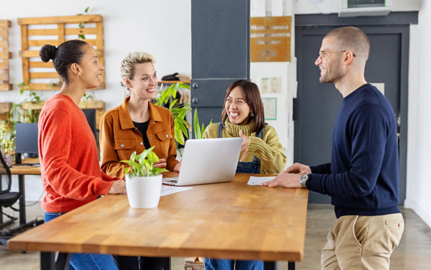 Coworkers chatting around a high table in an open workspace.