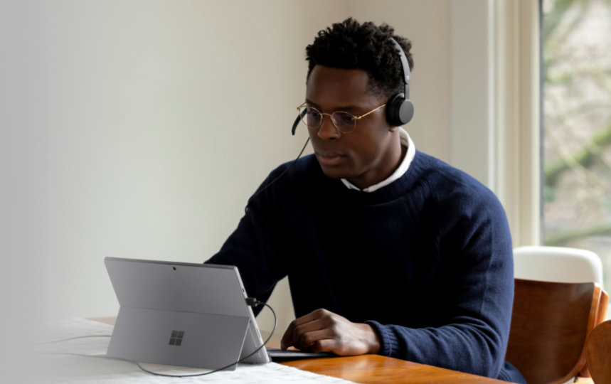 Un adulte dans une salle, qui porte un casque USB Microsoft Modern et utilise une Surface Pro