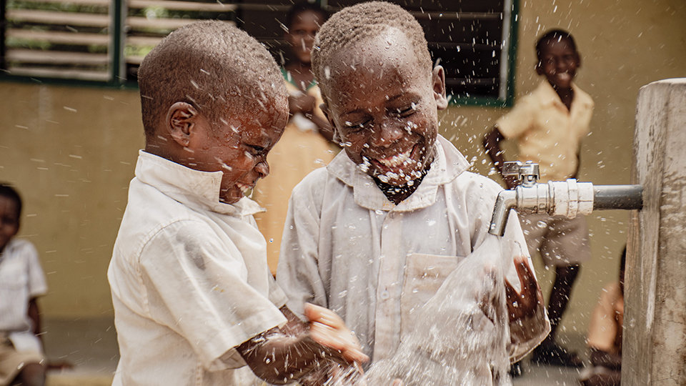 Two children happily playing with water from a faucet.