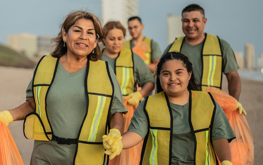 A group of people wearing safety vests working together to clean up a beach.