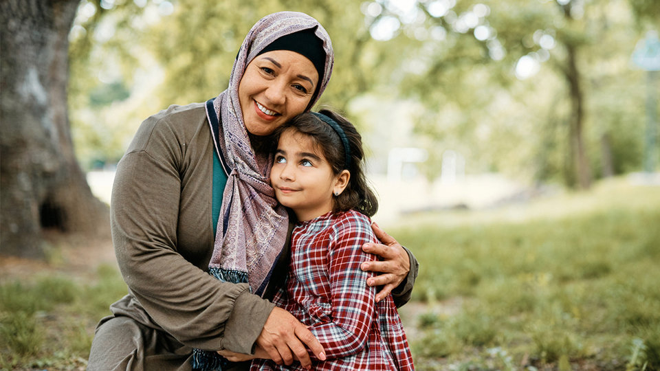 A woman embraces a child in a peaceful park setting.