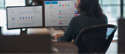 一位女士坐在放着两台显示器的桌旁。