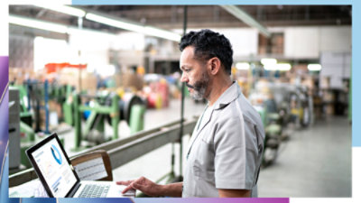 Person using a laptop at a workstation overlooking a large industrial facility.