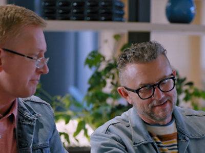 Two people wearing glasses sit together in a modern indoor setting.