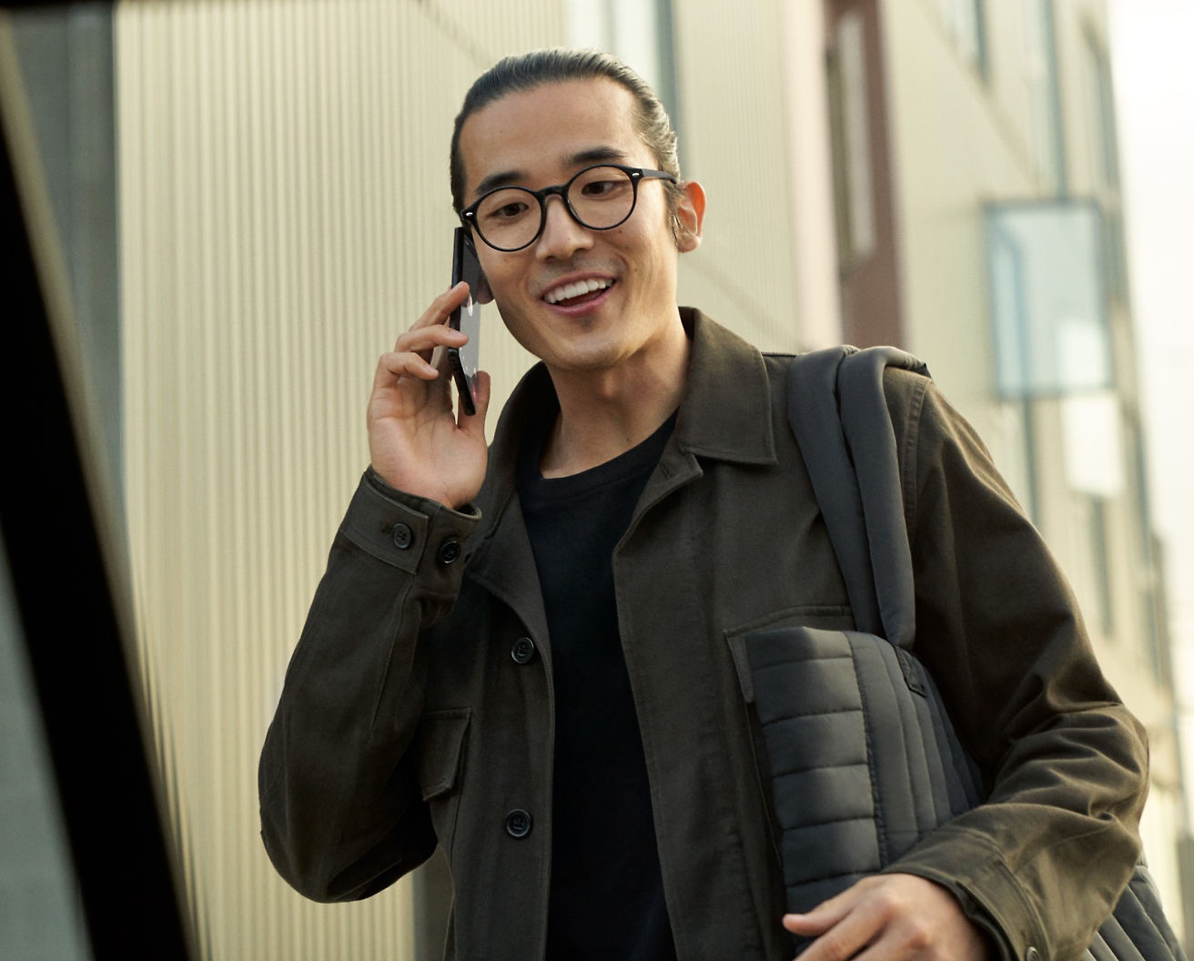 Een persoon met een bril die een mobiele telefoon vasthoudt en glimlacht