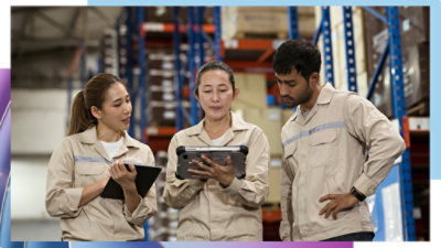 Three workers in an industrial facility reviewing information on tablets together.