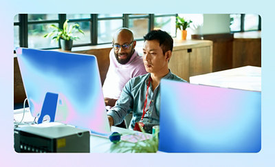 Two people collaborating at desktop computers in an office