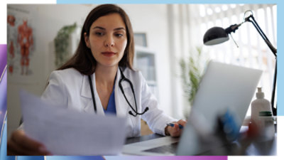 Healthcare professional wearing a white coat and stethoscope, reviewing documents beside an open laptop.
