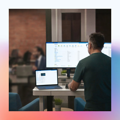 Arka planda iş arkadaşları varken modern bir ofisteki bilgisayarda çalışan bir erkek.