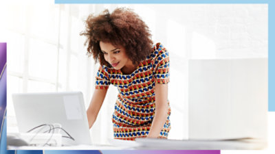 Person leaning over a laptop while working at a desk in a well-lit office space.