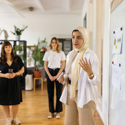 A person presenting beside a wall display while two colleagues stand in the background