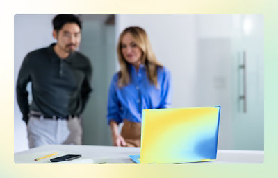 A man and woman standing in front of a laptop with a yellow and blue background.