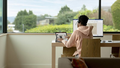 A person wearing a hoodie sitting at a desk using a laptop.