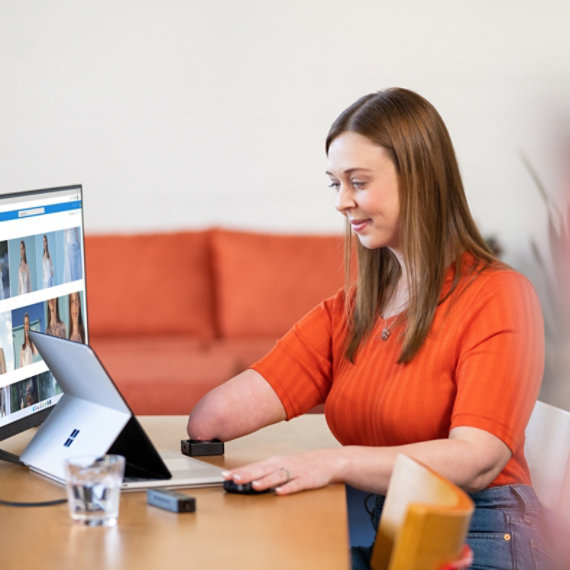 A woman uses an adaptive accessory while using a Surface laptop.