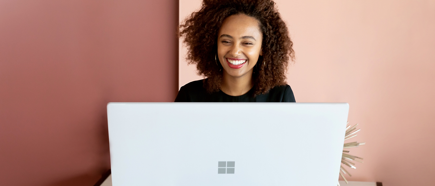 A woman is smiling while working on a laptop.