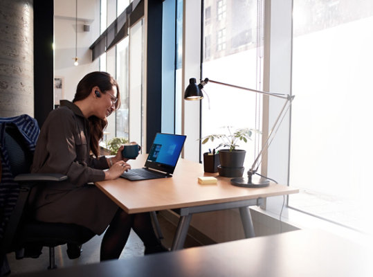 Mujer sentada en un escritorio con un portátil abierto que muestra Windows 10 Pro en la pantalla