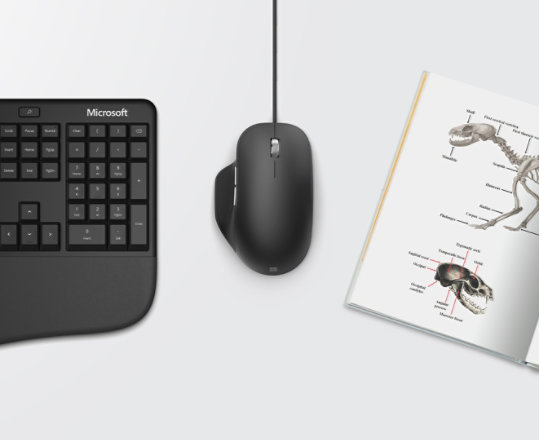 Microsoft ergonomic keyboard and mouse beside a book.