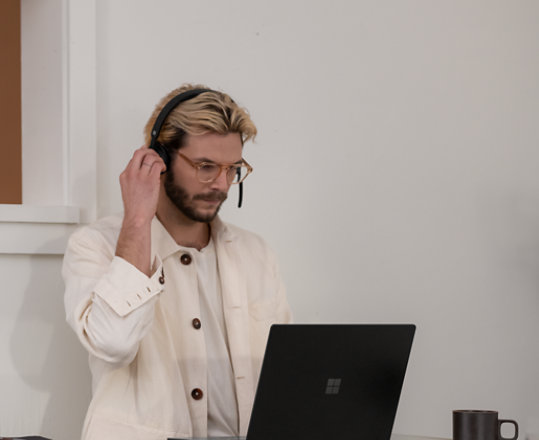 Henkilö käyttämässä Microsoft Modern Wireless Headset -kuulokkeita ja katsomassa laitetta.