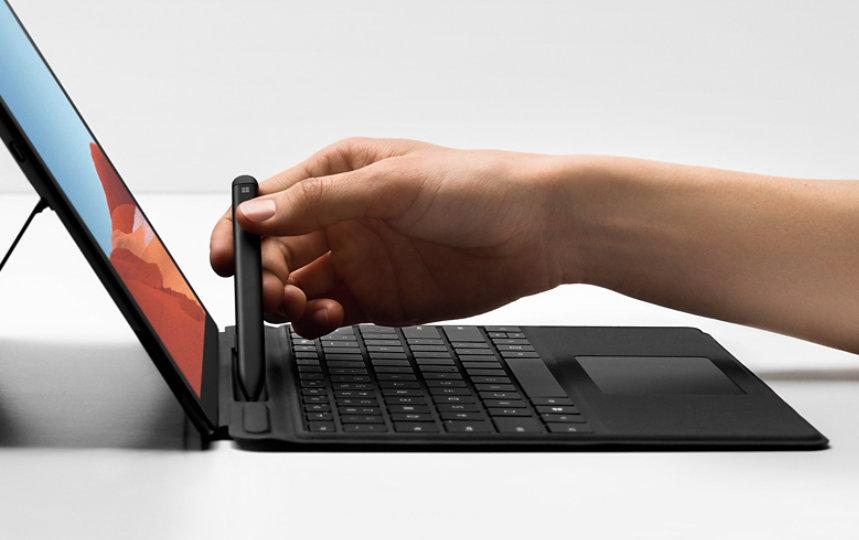 A person docking the Slim Pen in the Signature Keyboard attached to a Surface Pro X.