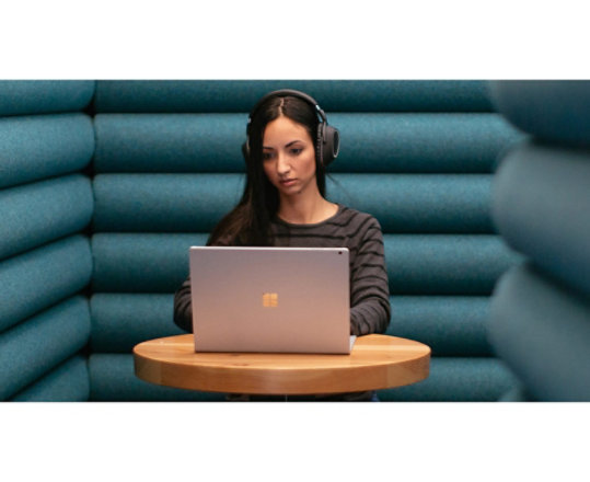 A woman sits quietly in solitude while wearing headphones as she works on her Windows 10 laptop.