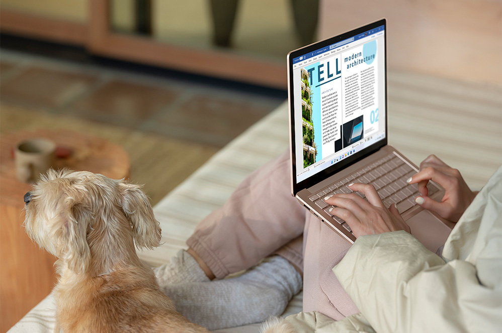 A user sits on the couch while typing on her Surface Laptop 4.