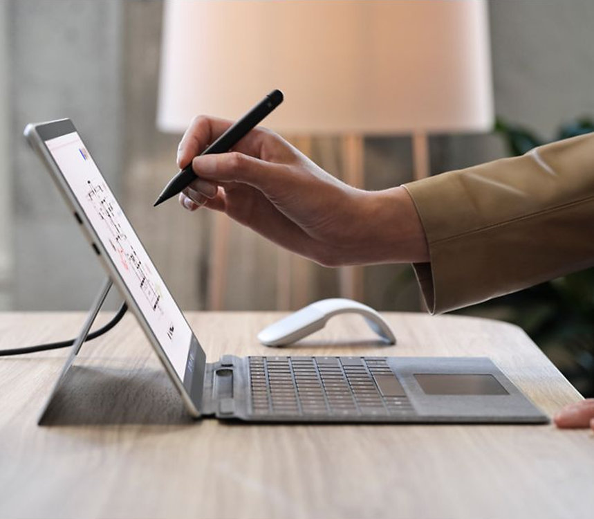 La mano di una persona tiene una penna Surface Slim Pen 2 per le aziende davanti allo schermo di un dispositivo Surface.