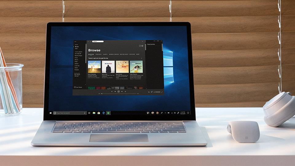 A Surface Arc Mouse on a desk next to an open Surface device.