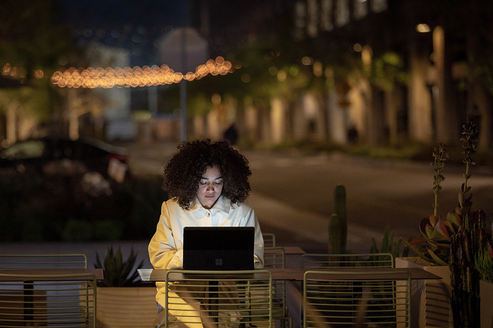 A woman uses Surface Pro X with the Signature Keyboard attached while sitting outside.
