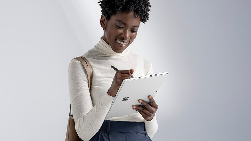 A smiling woman writing with a Slim Pen 2 on a Surface device.