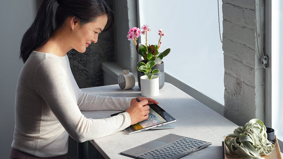 A person seated at a desk working with Surface Slim Pen 2 and Surface Pro Signature Keyboard.