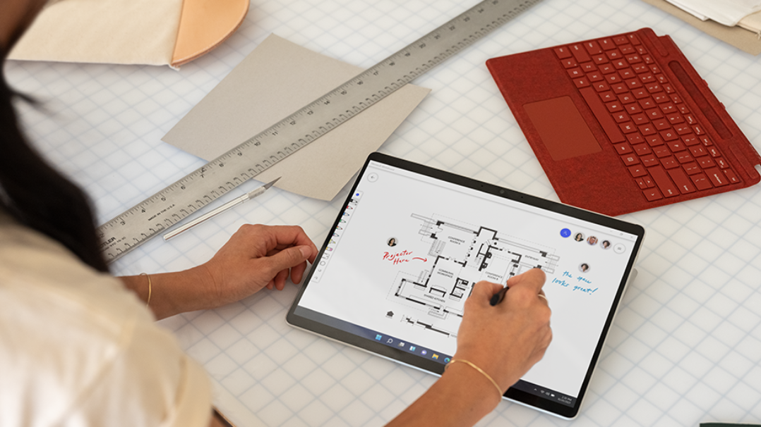 Person sitzt an einem Schreibtisch und schreibt mit einem Surface Pen auf einem Surface Pro X-Gerät