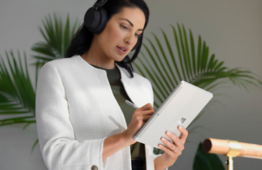 A person wearing headphones and holding Surface Go 3 for Business and Surface Slim Pen 2 for Business.