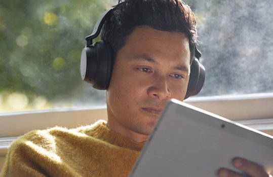 Man looking at the Go 3 while wearing headphones and sitting near a window.