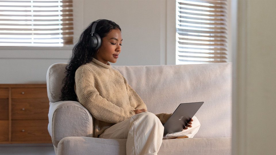 Person wearing Surface Headphones+ and holding a Surface device.