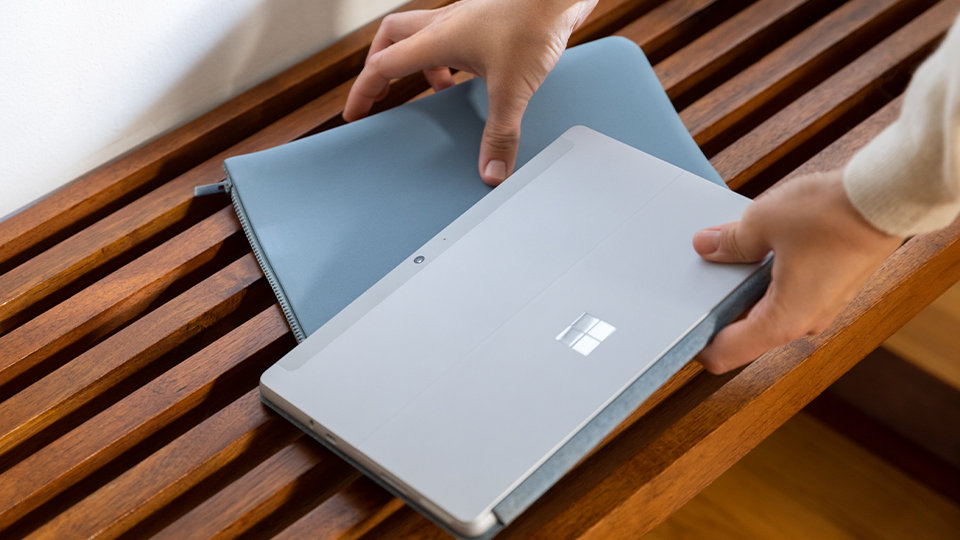A person picks up a Surface Go Sleeve in Ice Blue and a Surface Go.