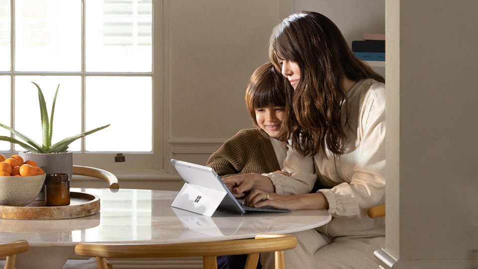 Zwei Personen sitzen an einem Tisch und verwenden ein Surface Go 2-Gerät mit einem Surface Go Type Cover.