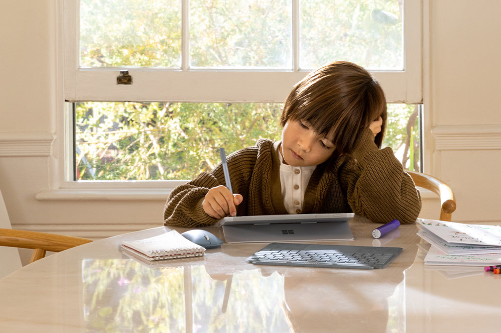 Ein Kind sitzt am Tisch und hält den Surface Go 2-Bildschirm