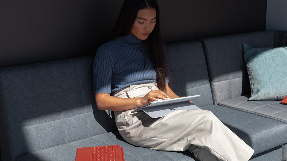 A person uses Surface Pro 7 while sitting on a sofa.